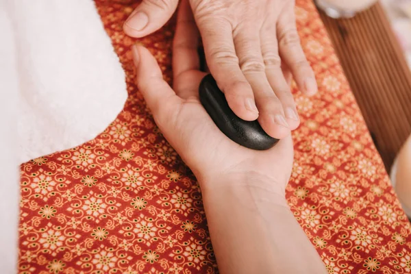 Vista cortada de massagista fazendo massagem de pedra quente para a mulher no salão de spa — Fotografia de Stock