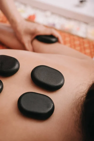 Vista recortada de masajista haciendo masaje de piedra caliente a la mujer en el salón de spa - foto de stock