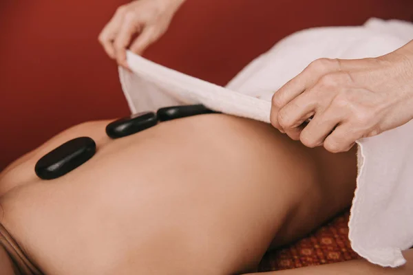 Vue recadrée du masseur faisant massage aux pierres chaudes à la femme dans le salon de spa — Photo de stock