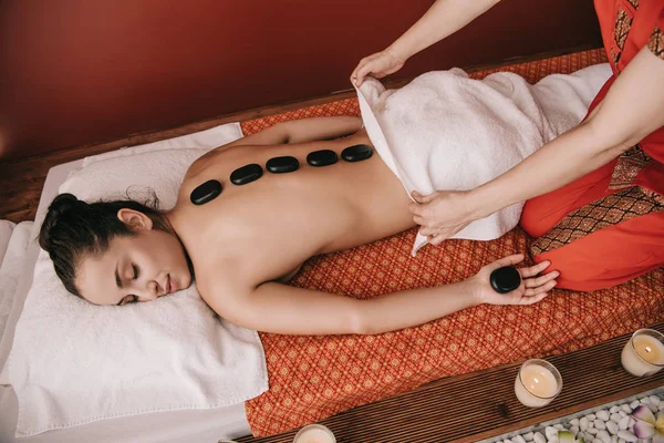 Vue recadrée du masseur faisant massage aux pierres chaudes à la femme dans le salon de spa — Photo de stock