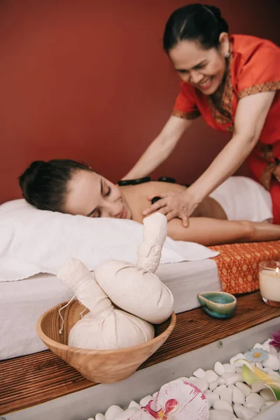 Foco seletivo de bolas de ervas e massagista asiático fazendo massagem de pedra quente — Fotografia de Stock