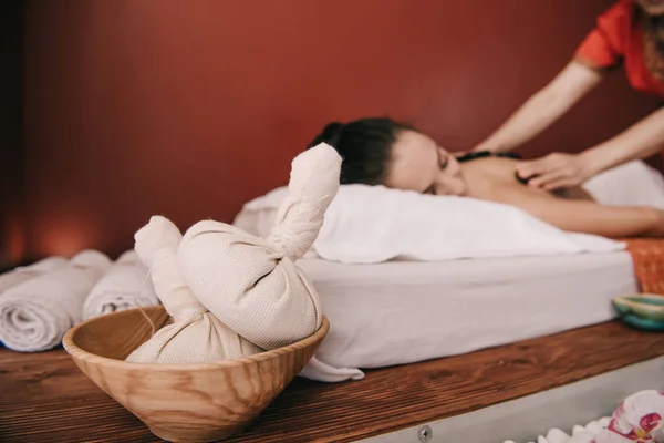 Foco seletivo de bolas de ervas e massagista asiático fazendo massagem de pedra quente — Fotografia de Stock