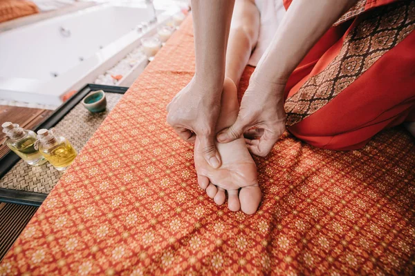 Vista recortada de masajista haciendo masaje de pies a mujer en salón de spa - foto de stock