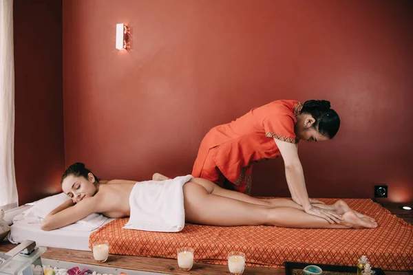 Vista lateral de masajista asiático haciendo masaje de pies a mujer en salón de spa - foto de stock