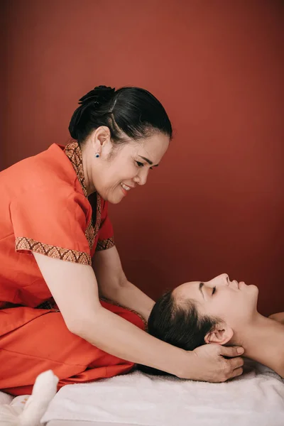 Vue latérale de masseur asiatique faisant massage du cou à la femme dans le salon de spa — Photo de stock