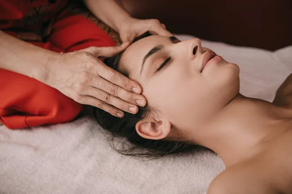 Vue recadrée du masseur faisant massage du visage à la femme dans le salon de spa — Photo de stock