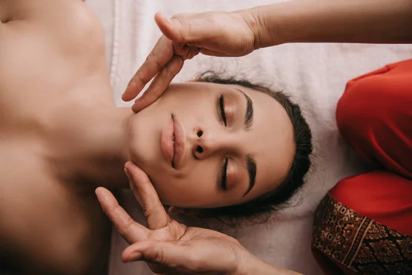 Cropped view of masseur doing face massage to woman in spa salon — Stock Photo