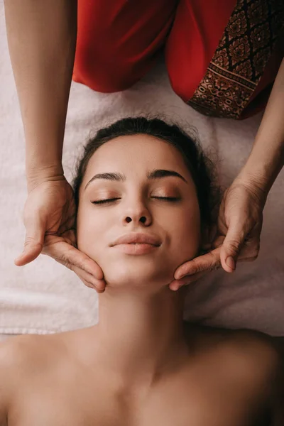 Vue recadrée du masseur faisant massage du visage à la femme dans le salon de spa — Photo de stock
