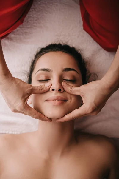 Vue recadrée du masseur faisant massage du visage à la femme dans le salon de spa — Photo de stock