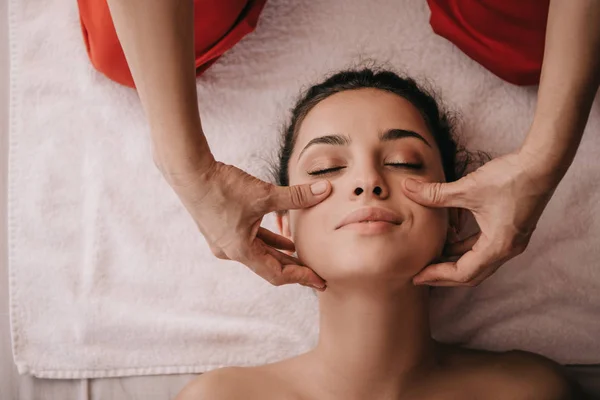 Vista recortada de masajista haciendo masaje facial a mujer en salón de spa - foto de stock