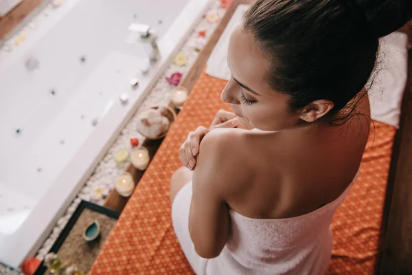 Vista de ángulo alto de la atractiva mujer con los ojos cerrados en la toalla sentado en la alfombra de masaje - foto de stock