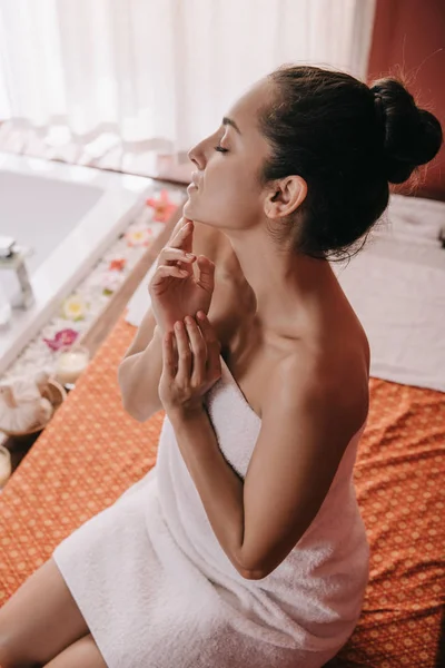 Vista ad alto angolo di donna attraente con gli occhi chiusi in asciugamano seduto sul tappeto da massaggio — Foto stock
