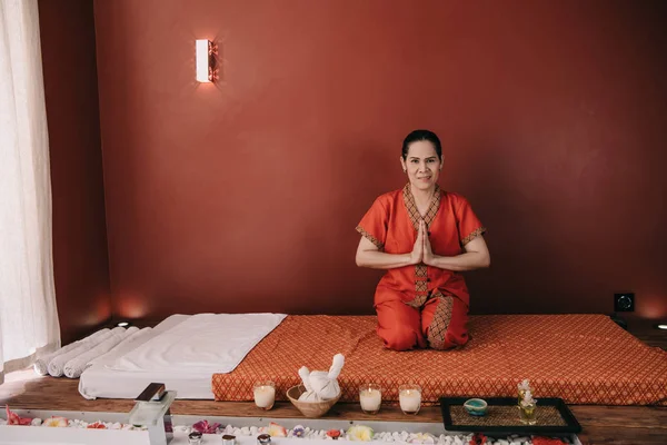 Asian masseur in red costume smiling and showing greeting hands — Stock Photo