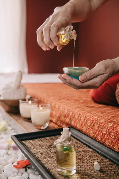 Обрізаний вид масажиста, що сидить на масажному килимку і наливає олію аромату в миску — стокове фото