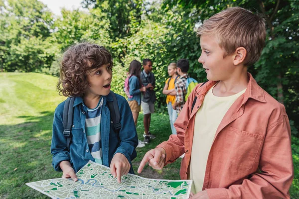 Enfoque selectivo de chicos lindos señalando con los dedos en el mapa cerca de amigos - foto de stock