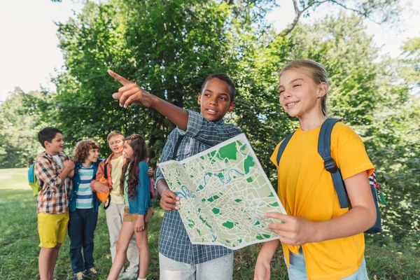 Selective focus of african american boy pointing with finger near kid holding map — Stock Photo