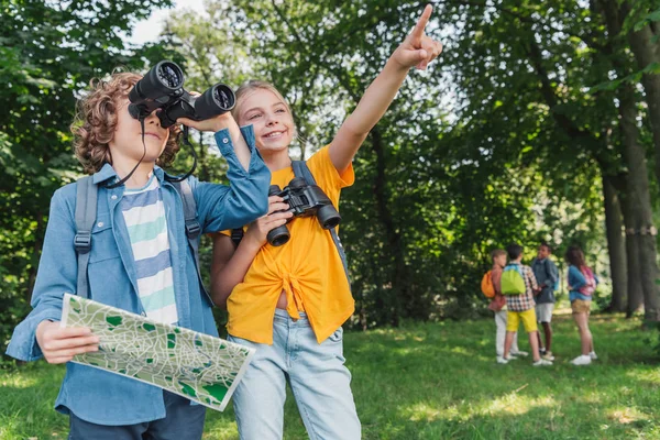 Enfoque selectivo de niño feliz señalando con el dedo cerca de amigo sosteniendo mapa y mirando a través de prismáticos - foto de stock