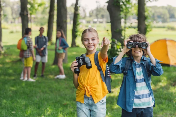 Selective focus of kid looking through binoculars near friend pointing with finger — Stock Photo
