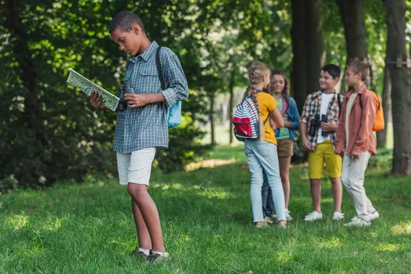 Enfoque selectivo de niño afroamericano mirando el mapa cerca de amigos - foto de stock