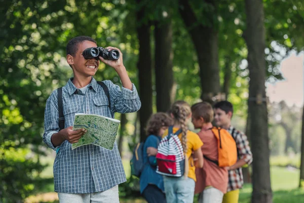 Selective focus of happy african american kid looking through binoculars near friends — Stock Photo