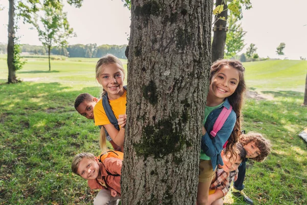 Grupo multicultural feliz de crianças sorrindo perto de tronco de árvore — Fotografia de Stock