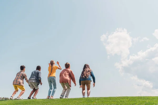 Back view of multicultural kids jumping on green grass — Stock Photo