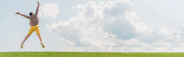 Tiro panorâmico de menino pulando e gesticulando contra o céu azul — Fotografia de Stock