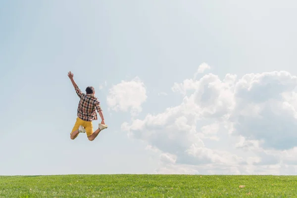 Back view of boy with outstretched hand jumping against blue sky — Stock Photo