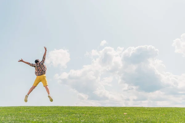 Вид сзади мальчика, прыгающего и жестикулирующего на фоне голубого неба — стоковое фото