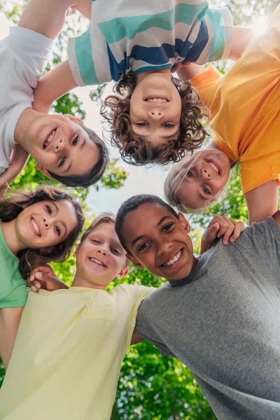 Вид снизу веселых мультикультурных детей, смотрящих на камеру в парке — стоковое фото