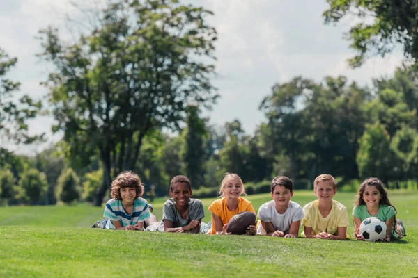 Niños multiculturales felices acostados en la hierba con pelotas - foto de stock