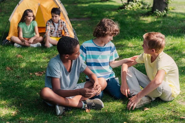 Enfoque selectivo de chicos multiculturales sentados en la hierba - foto de stock