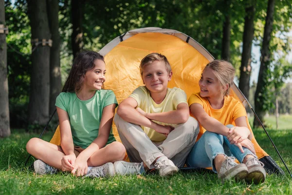 Garçon heureux assis avec des amis adorables près du camp — Photo de stock