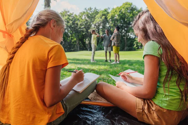 Enfoque selectivo de los niños que escriben en cuadernos cerca del campamento - foto de stock