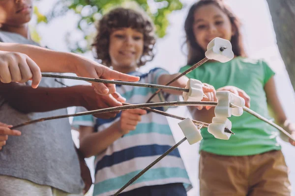 Foyer sélectif de guimauves douces en bâtons près des enfants multiculturels mignons — Photo de stock