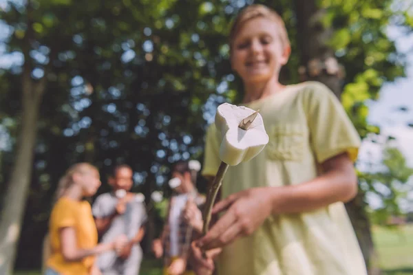 Selective focus of happy boy holding sweet marshmallow on stick near friends — Stock Photo