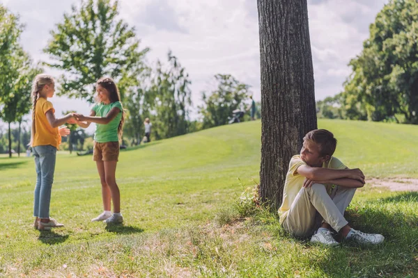 Selektiver Fokus trauriger Kinder, die in der Nähe von Baumstämmen sitzen und Kinder betrachten — Stockfoto