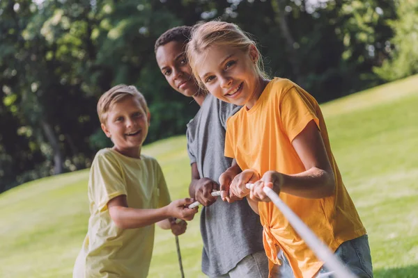 Selective focus of happy multicultural kids competing in tug of war — Stock Photo