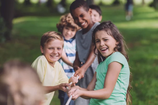 Selective focus of cheerful multicultural kids competing in tug of war — Stock Photo