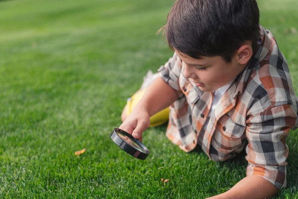 Selective focus of boy looking at grass through magnifier — Stock Photo