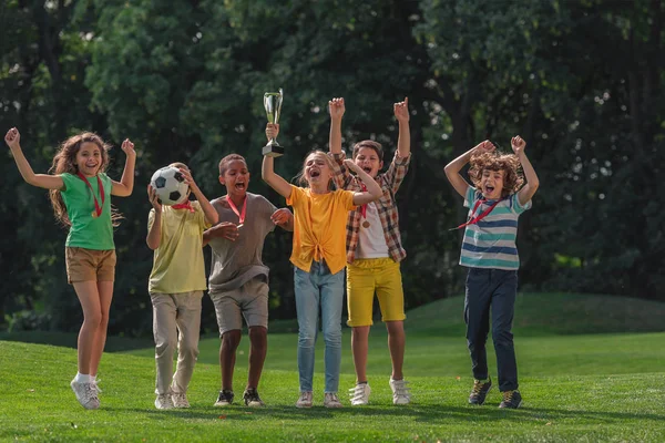 Fröhlicher multikultureller Kinderfußball und Trophäe im Park — Stockfoto