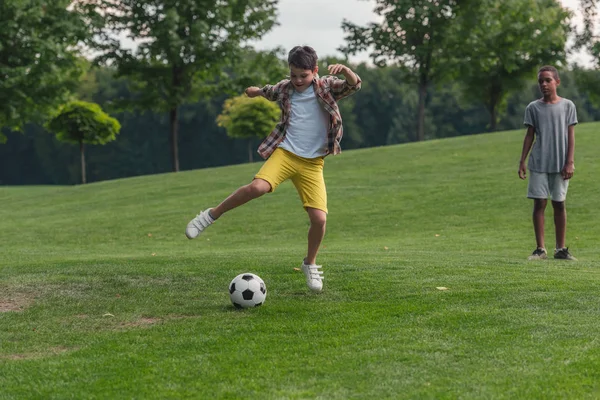 Lindo africano americano chico de pie en hierba cerca amigo jugando fútbol - foto de stock