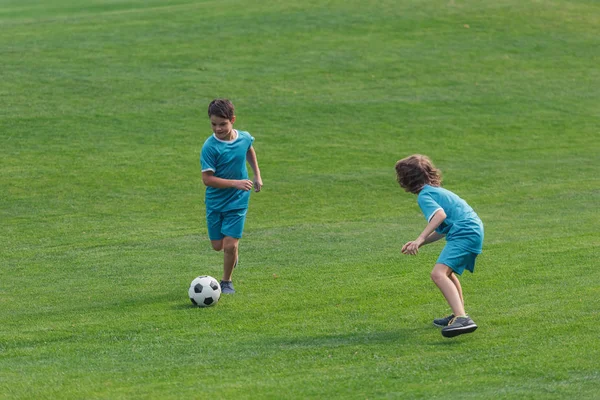Милые мальчики в спортивной одежде играют в футбол на траве — стоковое фото