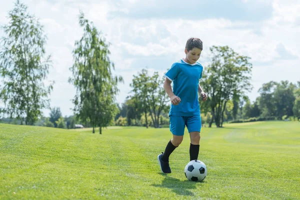 Lindo niño en ropa deportiva corriendo sobre hierba verde con el fútbol - foto de stock