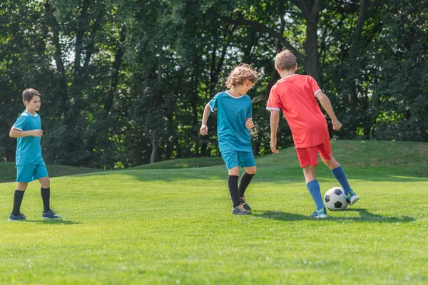 Mignon bouclé garçon jouer football avec amis sur herbe — Photo de stock