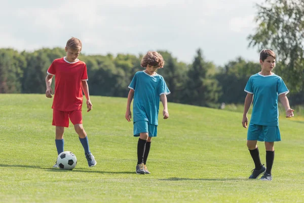 Курчавый мальчик играет в футбол с друзьями на зеленой траве — стоковое фото