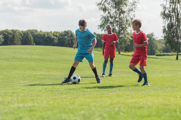 Cute multicultural friends playing football on green grass — Stock Photo