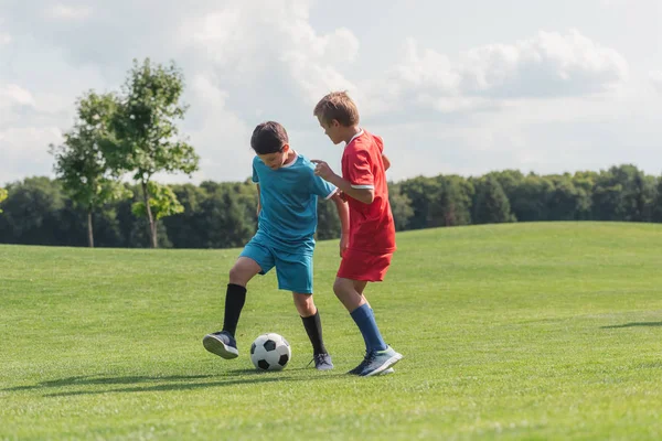 Милые друзья в спортивной форме играют в футбол на зеленой траве — стоковое фото