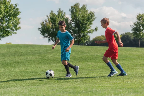 Amigos en ropa deportiva jugando fútbol sobre hierba verde - foto de stock