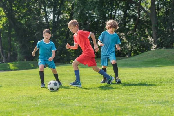 Cute friends in sportswear playing football on green grass in park — Stock Photo